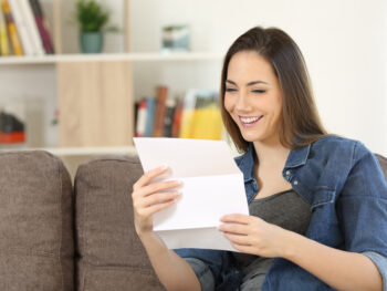 Happy woman reading a letter on a couch at home